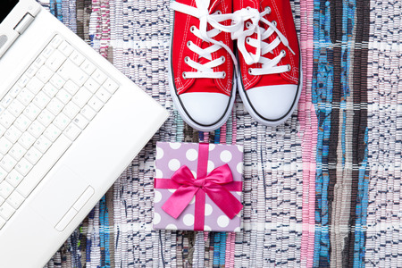 Red gumshoes and white computer near gift box on carpet backgroundの写真素材