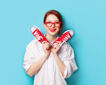 Beautiful redhead girl in white shirt with gumshoes on blue background.の写真素材