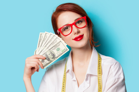 Portrait of redhead women in red glasses with money on blue backgroundの写真素材