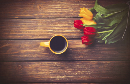 Cup of coffee and tulips on wooden table. Photo in old color image style.の写真素材