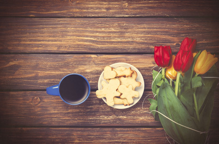 Cup of coffee and tulips with cookies on wooden background. Photo in old color image style.の写真素材