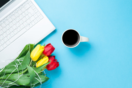 Cup of coffee and tulips with computer on blue background.の写真素材