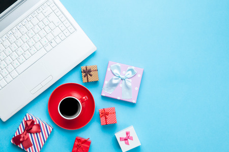 Cup of coffee with gift boxes and computer on blue backgroundの写真素材
