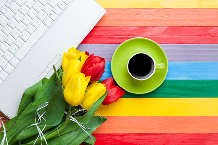 Cup of coffee with tulips and notebook on multicolored background.の写真素材