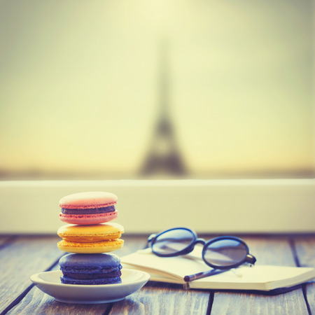 Macarons and little notebook with glasses on wooden table and Eiffel tower backgroundの写真素材