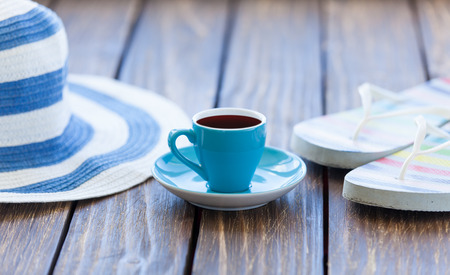 Cup of coffee and hat with flip flops on wooden table.の写真素材