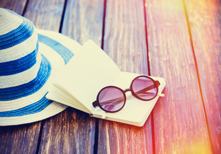 Sunglasses and hat with notebook on wooden table.の写真素材