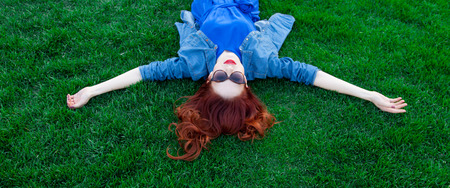 Beautiful redhead women lying down on green grass in summer time in the park.