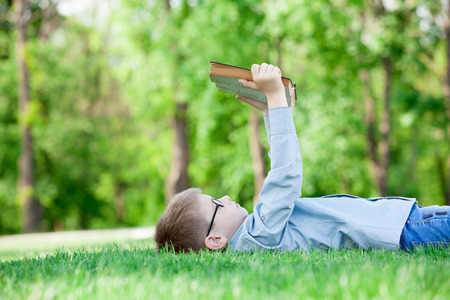 young boy with a book on green grass in the parkの写真素材