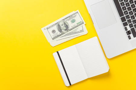 Notebook and laptop computer near dollars on yellow background