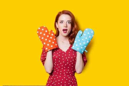 Surprised redhead girl in red polka dot dress and mittens on yellow background.の写真素材