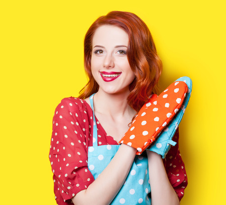 Smiling redhead girl in red polka dot dress and mittens on yellow background.の写真素材
