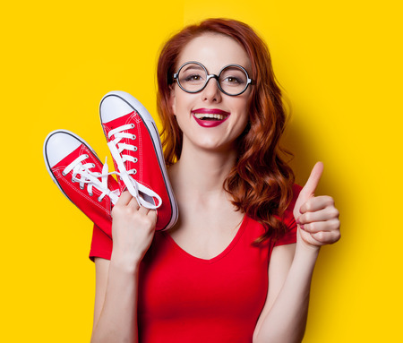 Young redhead girl in red dress with gumshoes on yellow background.の写真素材