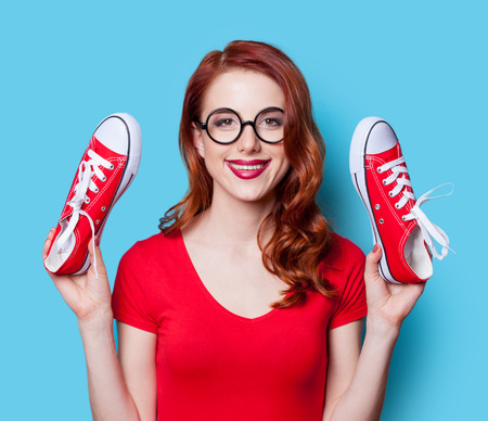 Smiling redhead girl in red dress with gumshoes on yellow background.の写真素材