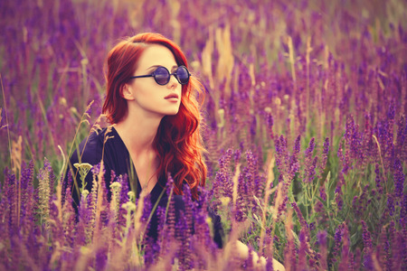 Portrait of a beautiful redhead girl with sunglasses on lavender field.