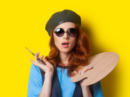 Surprised redhead painter with brush and palette on blue backgroundの写真素材