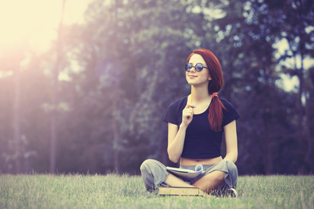 Young girl in indie style clothes with notebook on green grass in the parkの写真素材