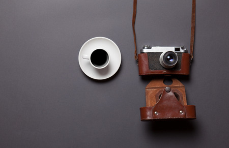 White cup of coffee and retro camera in leather case on grey backgroundの写真素材