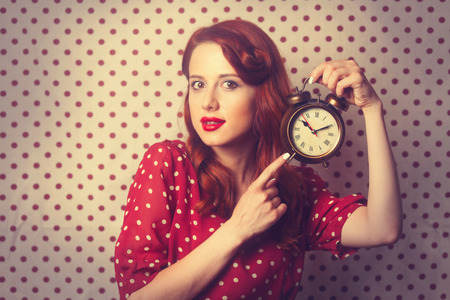 Portrait of a surprised redhead girl with alarm clock on Polka dot background.の写真素材