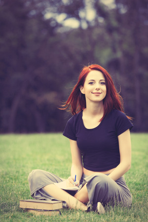 Young girl in indie style clothes with notebook on green grass in the parkの写真素材