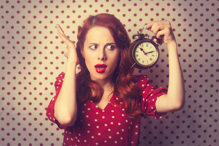 Portrait of a surprised redhead girl with alarm clock on Polka dot background.の写真素材