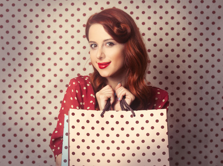 Portrait of a redhead girl with shopping bags on polka dot background.の写真素材