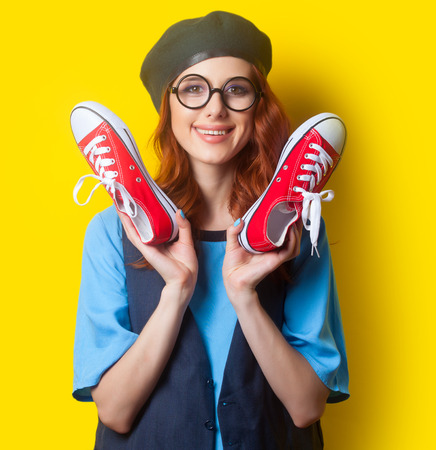Smiling redhead girl with red gumshoes on yellow background.の写真素材
