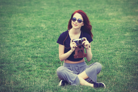 Young girl in indie style clothes with retro camera on green grass in the parkの写真素材