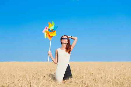 Redhead girl in white dress and wind toy at wheat field.の写真素材