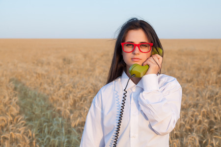 Young brunette girl with green dial handset on wheat field