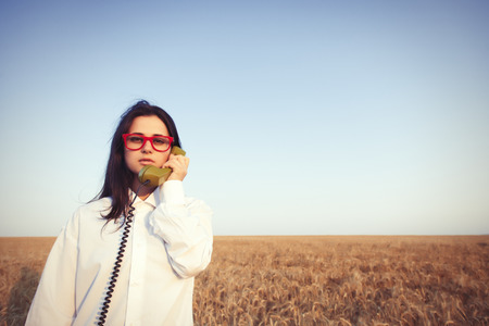 Young brunette girl with green dial handset on wheat field