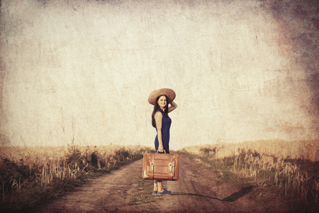 Brunette girl with suitcase at countryside roadの写真素材