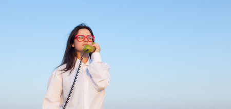 Young brunette girl with green dial handset on blue sky backgroundの写真素材