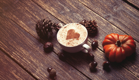 Cup of coffee with heart shape and pine cone with acorn and pumpkin on wooden backgroundの写真素材