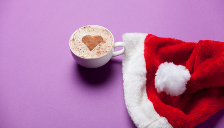 Cup of coffee and christmas hat on violet background.の写真素材