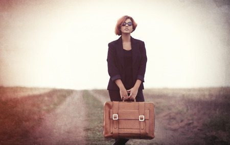 Style young women with suitcase at countryside outdoor. Photo in old color image style.の写真素材