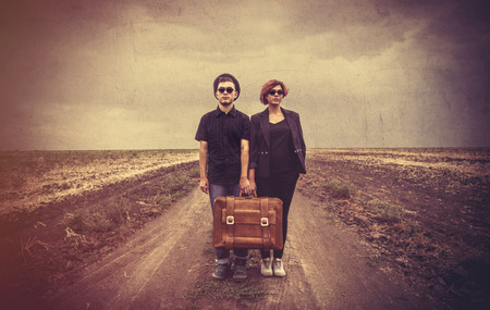Style young couple with suicase at countryside outdoor. Photo in old color image style.の写真素材