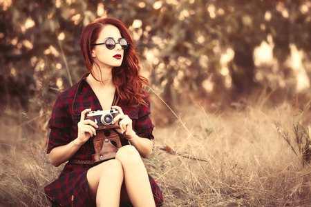 Beautiful girl in plaid dress retro camera and sunglasses at countrysideの写真素材