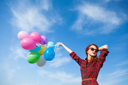 Beautiful girl in plaid dress with multicolored balloons on blue sky backgroundの写真素材