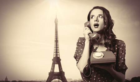 Surprised girl in polka dot dress with dial phone and Eiffel tower on background.の写真素材