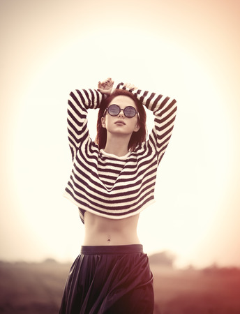 Portrait of a young redhead girl in sunglasses and striped sweater at outdoor in autumn timeの写真素材
