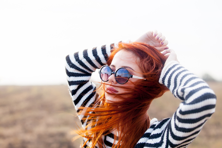 Portrait of a young redhead girl in sunglasses and striped sweater at outdoor in autumn timeの写真素材