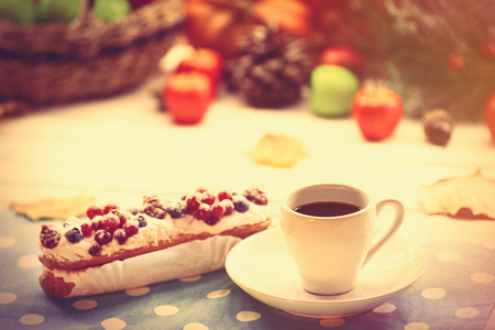 Eclair and cup of coffee on wooden table.