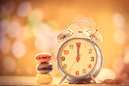 Alarm clock and french macarons on yellow autumn background.
