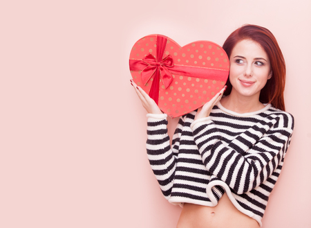Portrait of a young beautiful caucasian woman with heart shape box on pink backgroundの写真素材