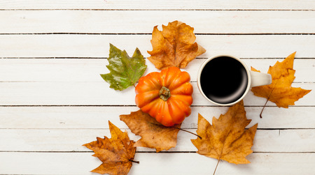 Cup of coffee and pumpkin with leafs on white wooden table
