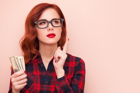 redhead girl in red tartan dress with money on pink background.の写真素材