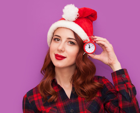 Redhead girl in Santa Claus hat with little alarm clock on violet backgroundの写真素材