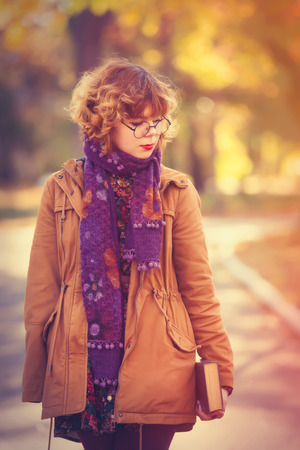 Young student girl with book in the autumn parkの写真素材