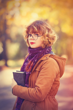 Young student girl with book in the autumn parkの写真素材
